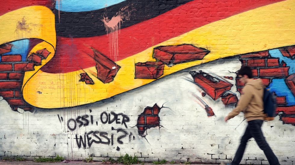 Ein Passant geht in Berlin an an einem Wandbild mit der deutschen Nationalflagge und dem Schriftzug "Ossi oder Wessi? vorbei. 