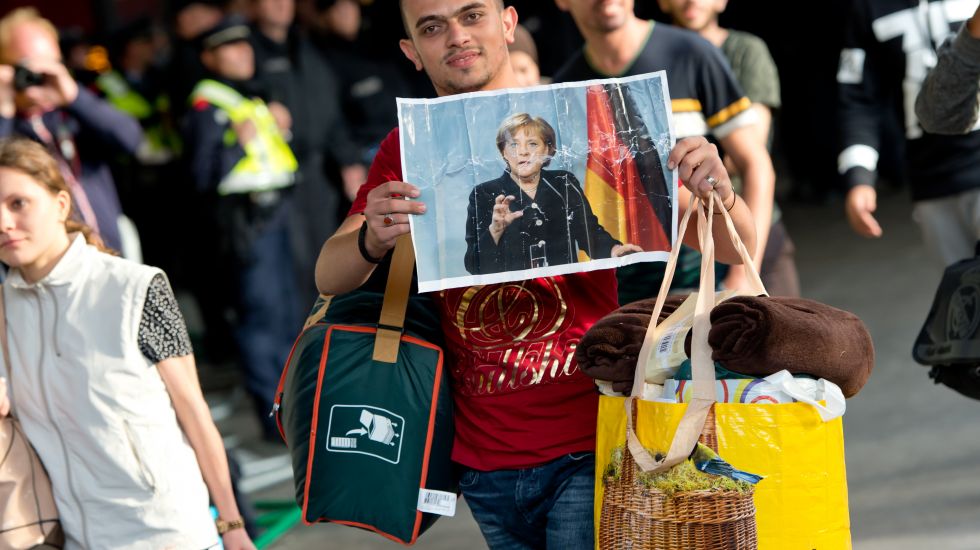 in Flüchtling, der kurz zuvor mit einem Zug angekommen ist, läuft am 05.09.2015 auf dem Hauptbahnhof in München (Bayern) über den Bahnsteig und hält dabei ein Foto von Angela Merkel in den Händen.
