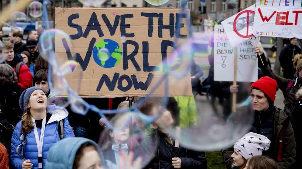 22.03.2019, Berlin: Seifenblasen schweben vor einem Plakat mit der Aufschrift „Save the World Now", das jugendliche Teilnehmer der Klima-Kundgebung "Friday for Future" am Invalidenpark halten.