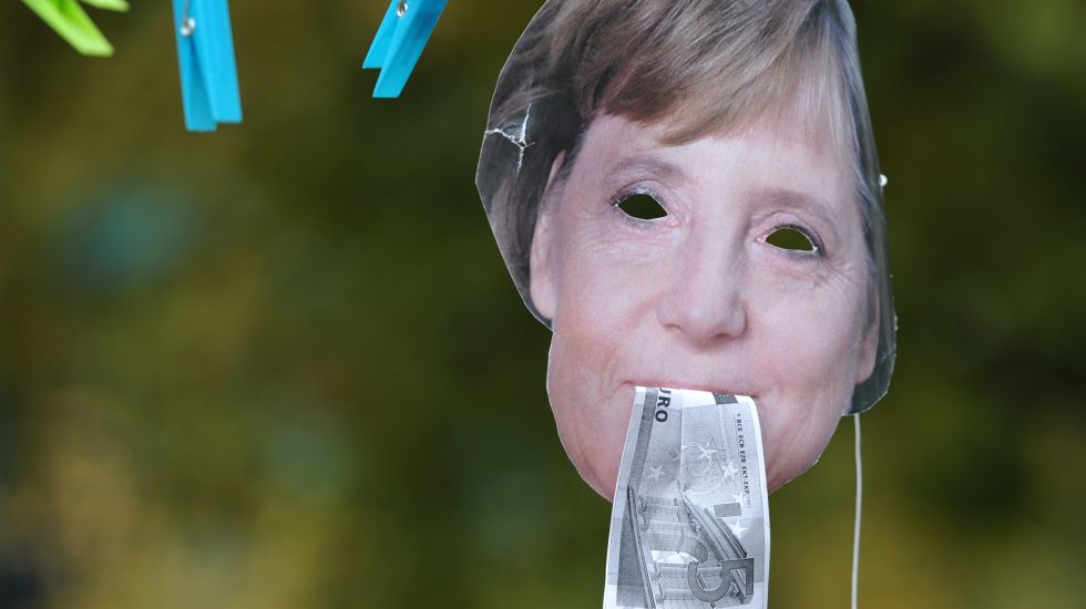 Eine Maske von Merkel mit Geld im Mund