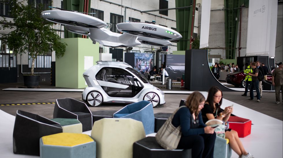 Zwei Besucherinnen sitzen bei der Green Tech Exhibition im Rahmen des Green Tech Festival im Hangar des ehemaligen Flughafen Tempelhof vor dem Modell eines Flug-Autos ("Pop.Up Next"), das von Audi und Airbus zusammen entwickelt wurde.