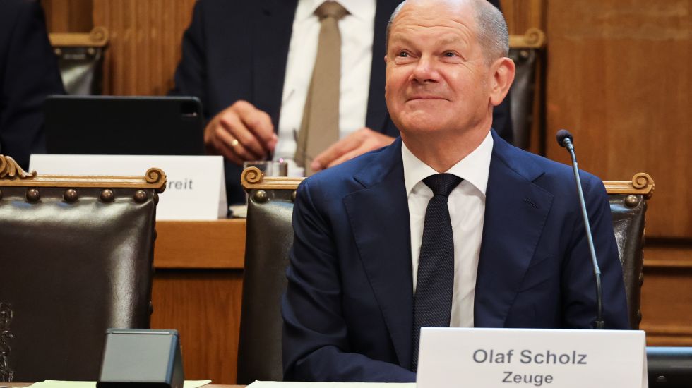 Bundeskanzler Olaf Scholz (SPD) sitzt auf seinem Platz auf der Senatsbank mit einem Plastikschild mit dem Text „Olaf Scholz Zeuge“ vor Beginn einer Sitzung des Parlamentarischen Untersuchungsausschusses „Cum-Ex“ im Plenarsaal der Hamburgischen Bürgerschaft im Rathaus.