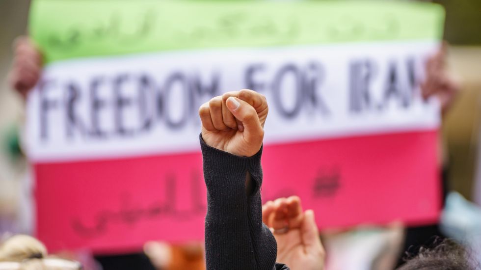 Eine Faust reckt sich vor einem Plakat mit der Aufschrift "Freedom for Iran"