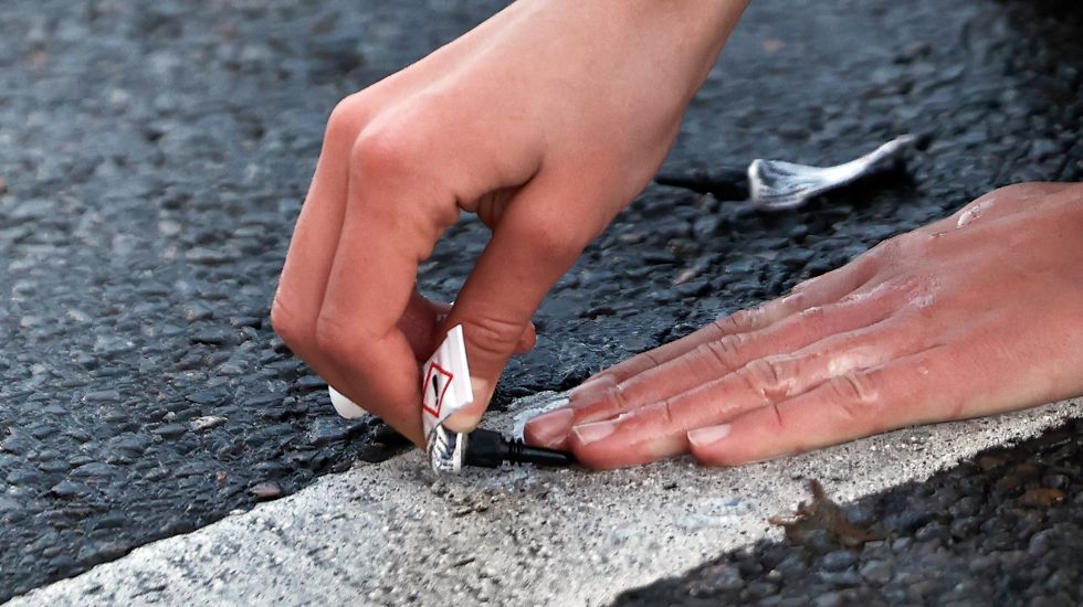 Ein Aktivist klebt seine Hand während einer Sitzblockade mit Sekundenkleber auf der Straße fest
