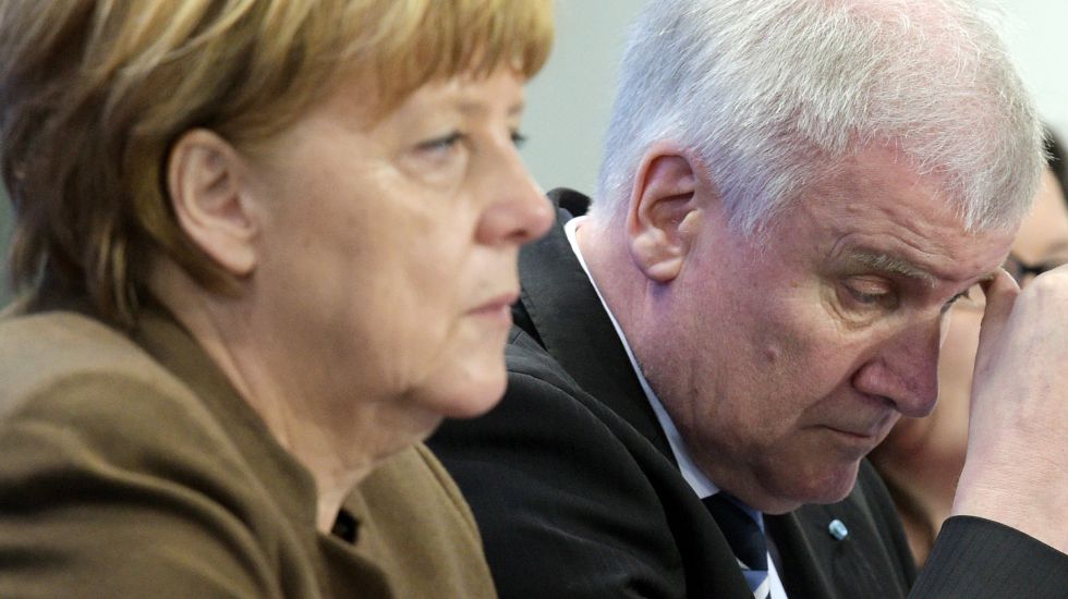 Angela Merkel und Host Seehofer sitzen nebeneinander. Seehofer runzelt die Stirn und fasst sich mit dem Daumen an die Augenbraue.