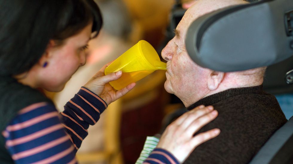 Eine Altenpflegerin hilft einem Pflegebedrüftigen beim Trinken.