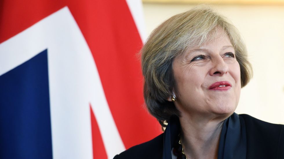 Theresa May lächelt. Hinter ihr die britische Flagge